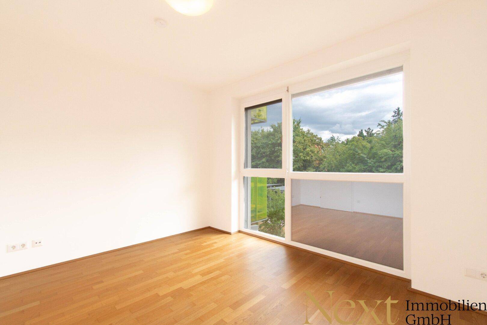 Helles Zimmer mit Parkettboden und großen Fenstern, die viel Tageslicht hereinlassen.