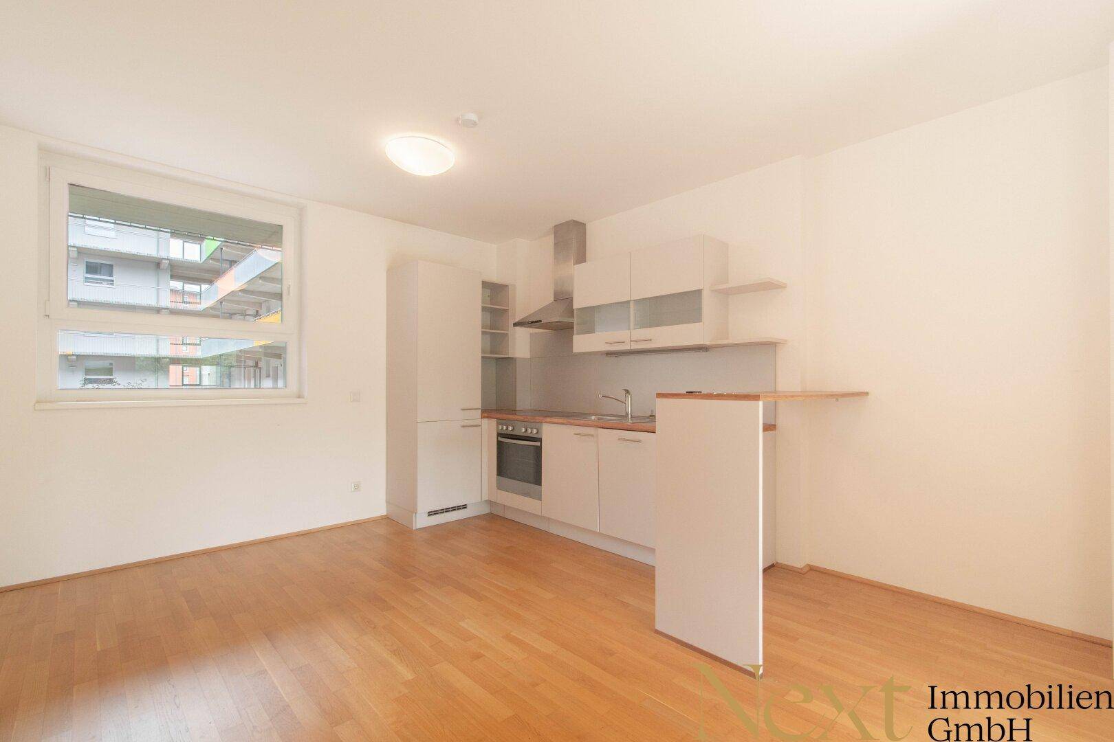 Offene Küchenzeile mit weißen Schränken, Holzboden und Fenster in einem hellen Raum.