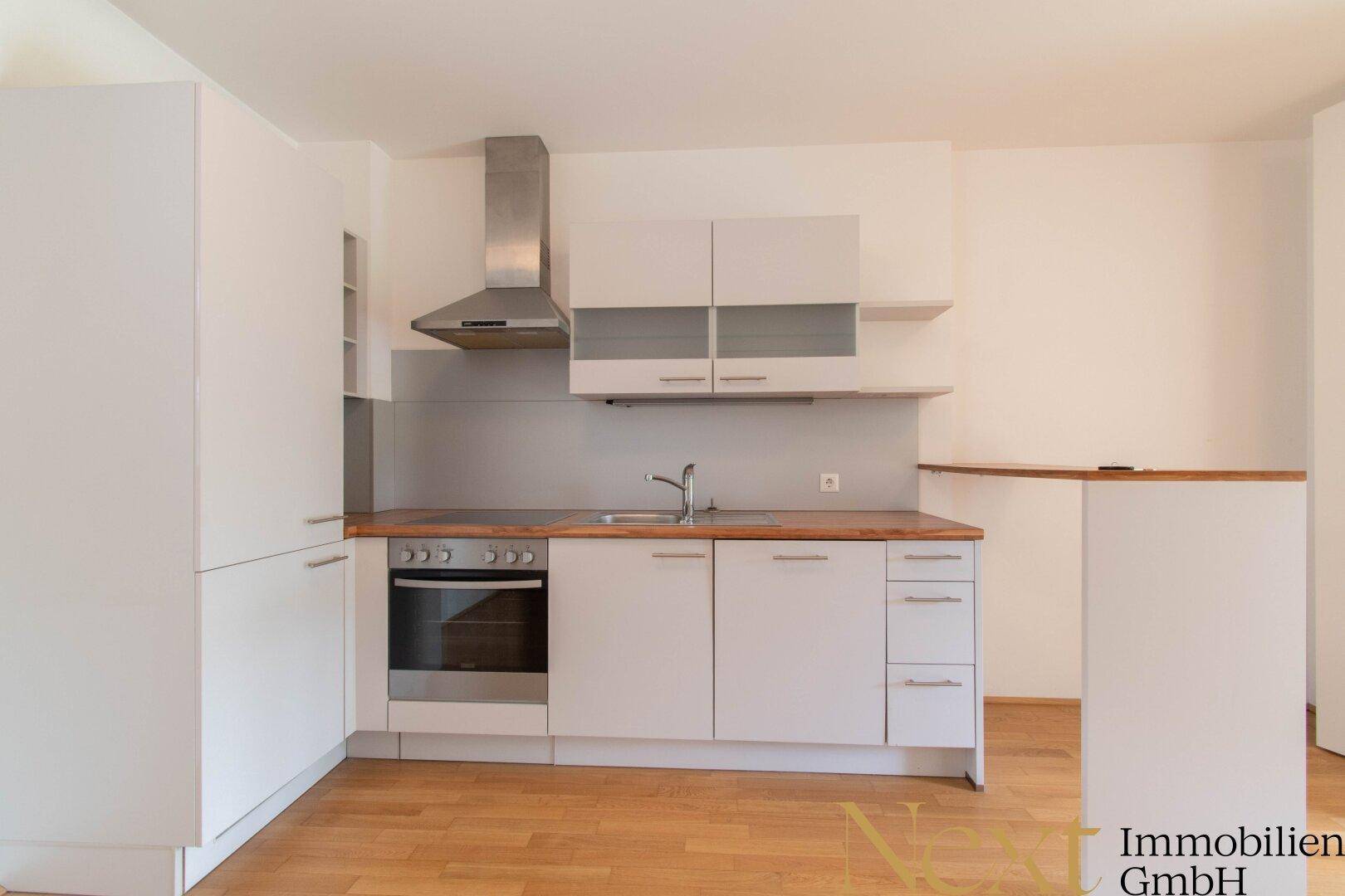 Moderne Küchenzeile mit weißen Fronten, Dunstabzugshaube und integriertem Backofen.