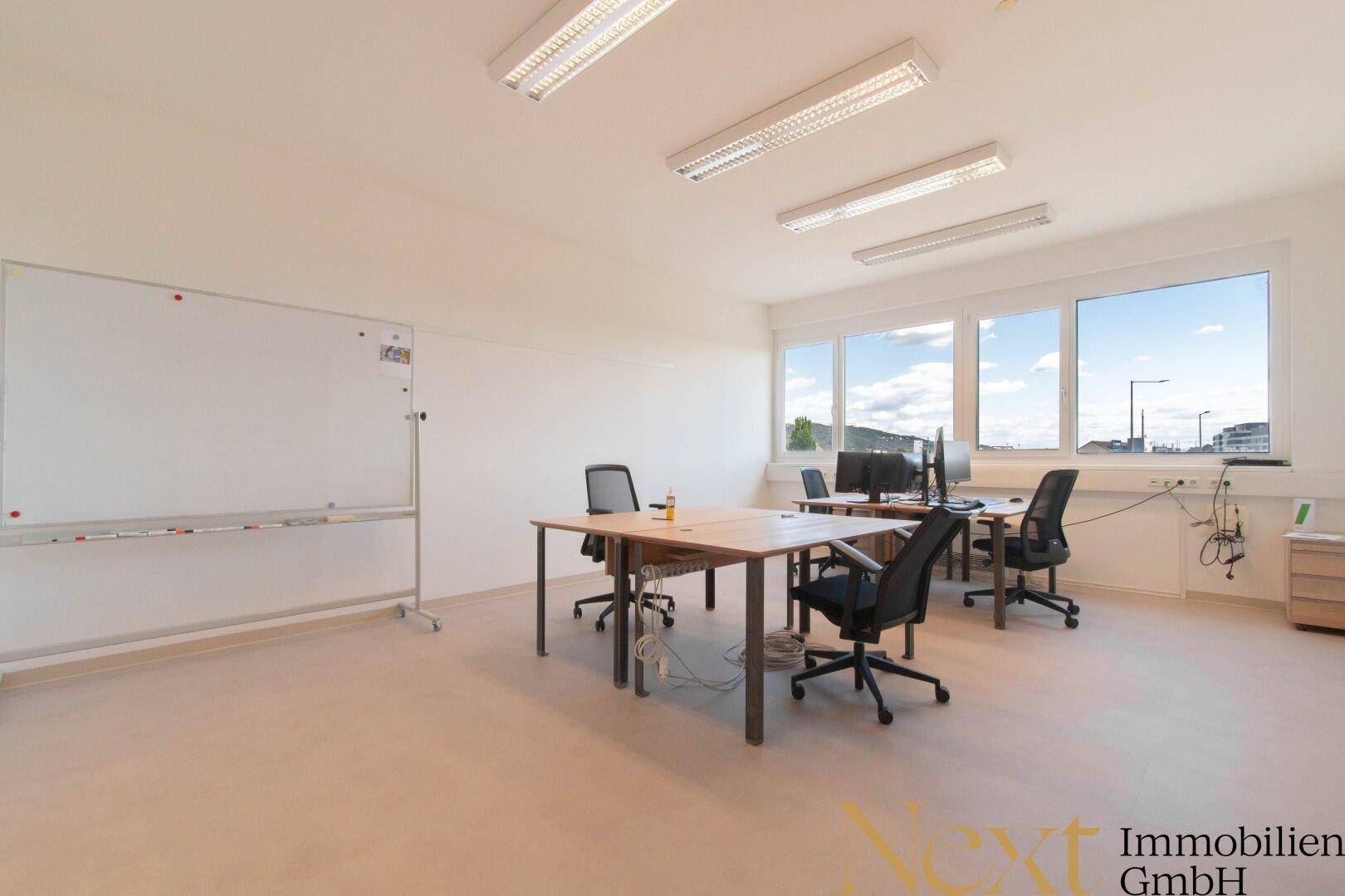 Geräumiges Büro mit mehreren Arbeitsplätzen und einer großen Whiteboard-Wand für Präsentationen.