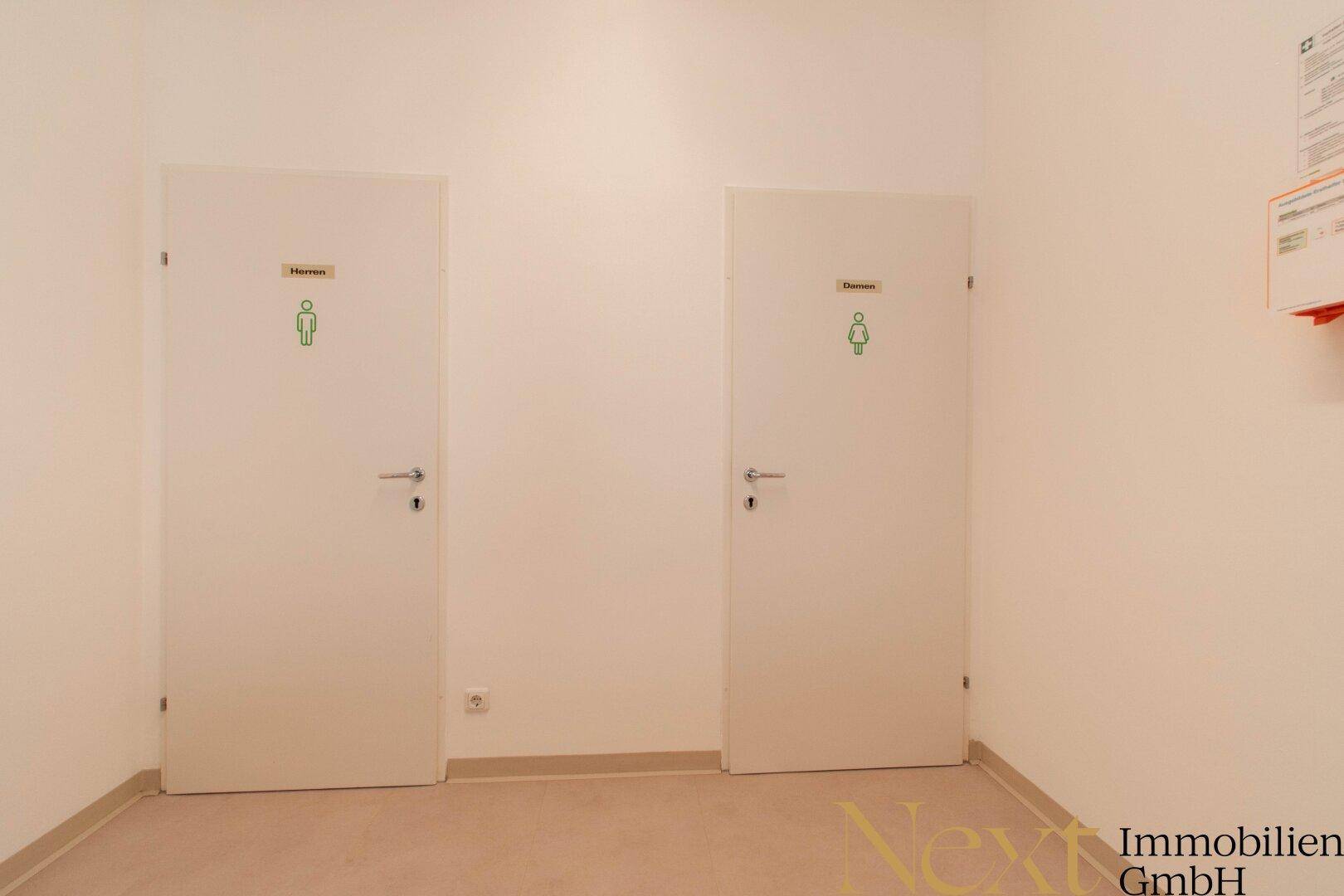 Zwei separate Toilettenkabinen mit klaren Beschriftungen für Damen und Herren.