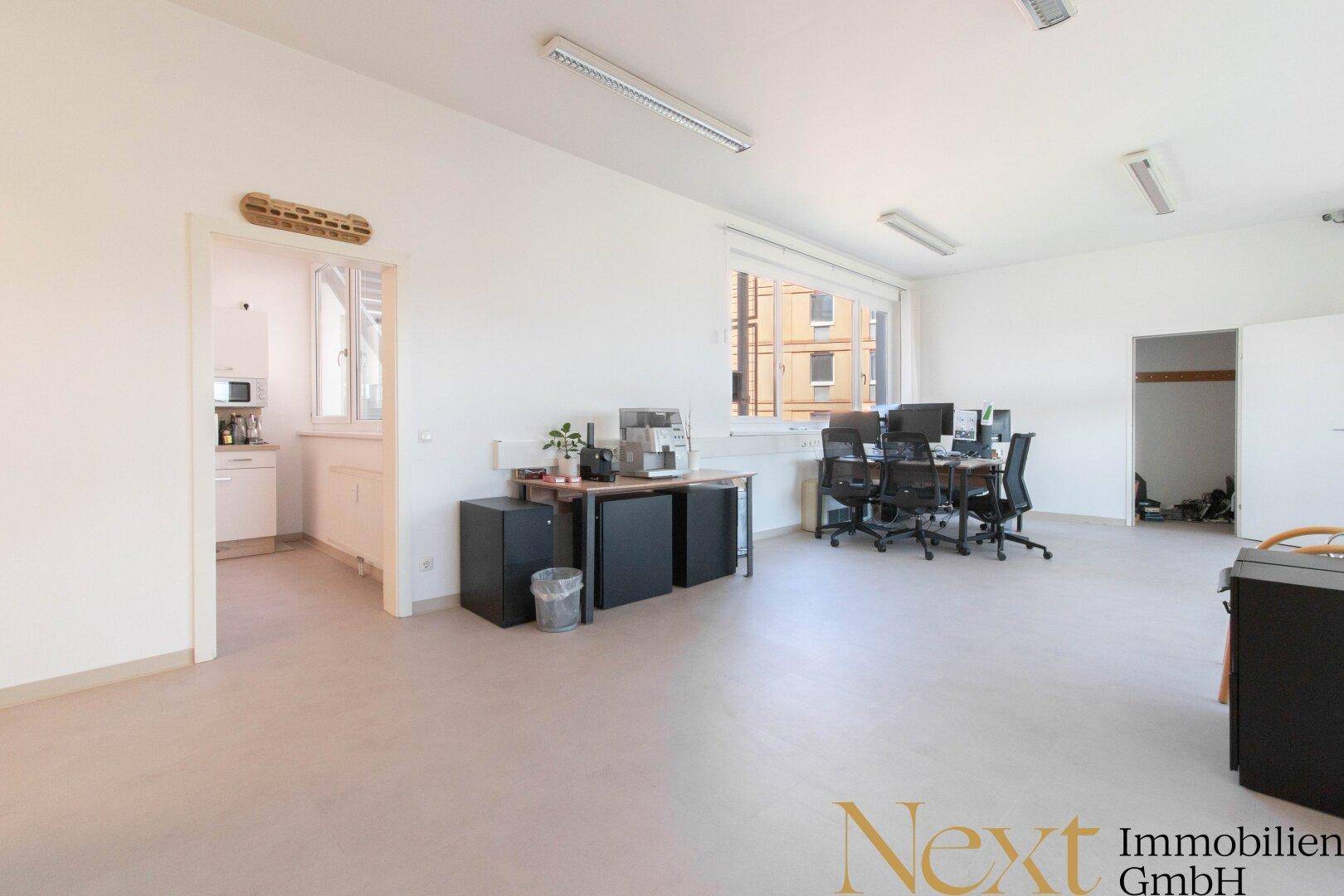 Großes Büro mit Arbeitsplätzen und Zugang zu einer kleinen Teeküche im Hintergrund.