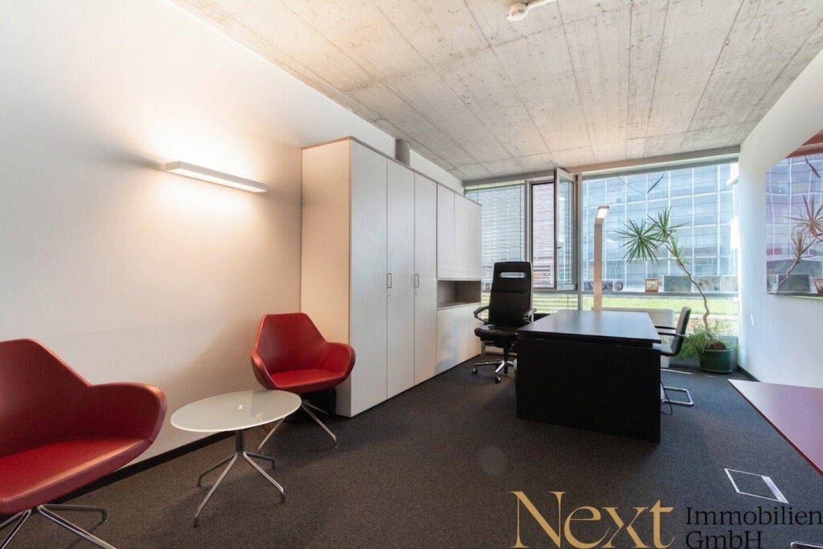 Modernes Büro mit Schreibtisch, bequemen Sesseln, weißen Schränken und großen Fenstern für viel Tageslicht.