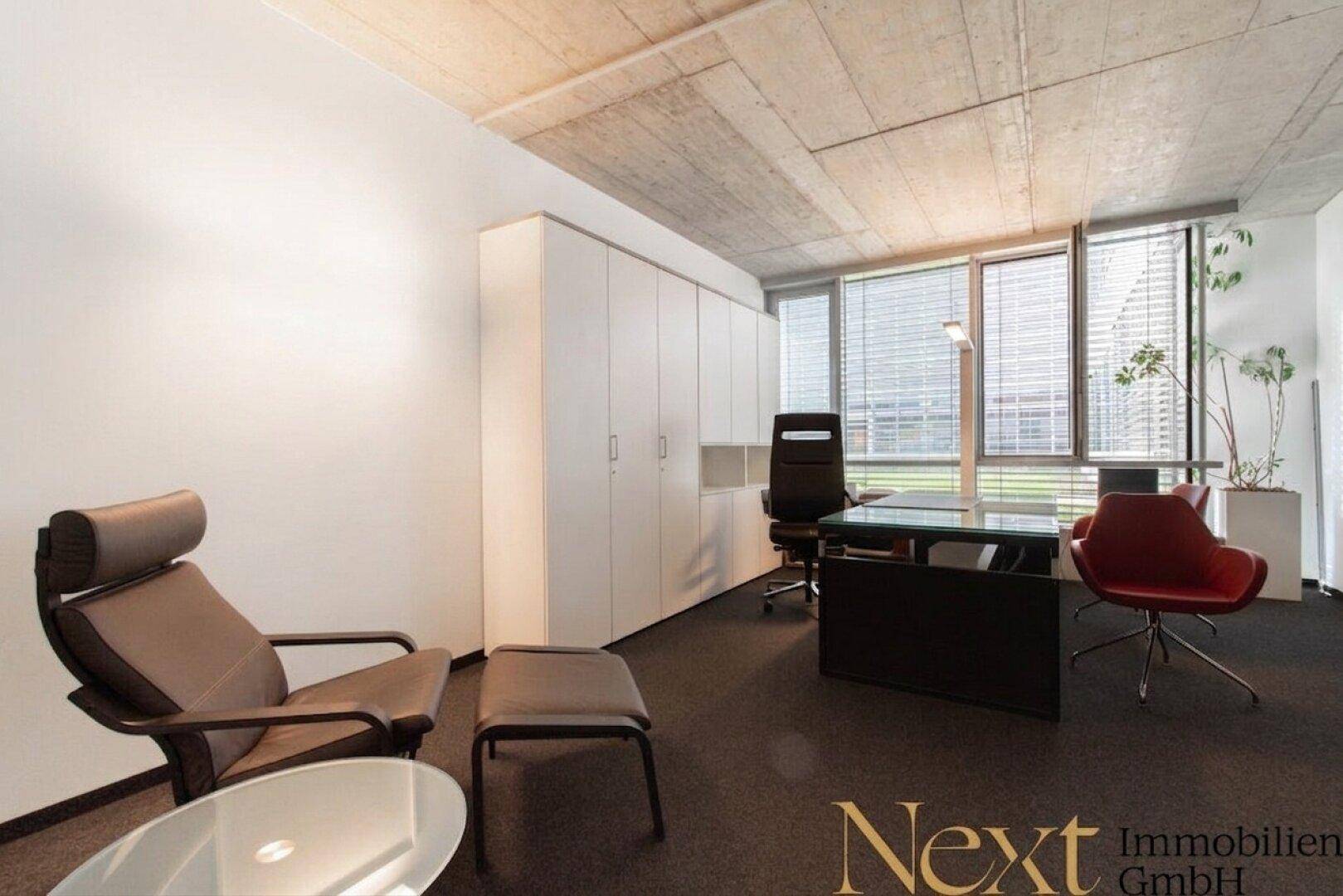 Elegantes Büro mit Schreibtisch, Loungesessel, weißen Schränken und großen Fenstern mit Blick nach draußen.