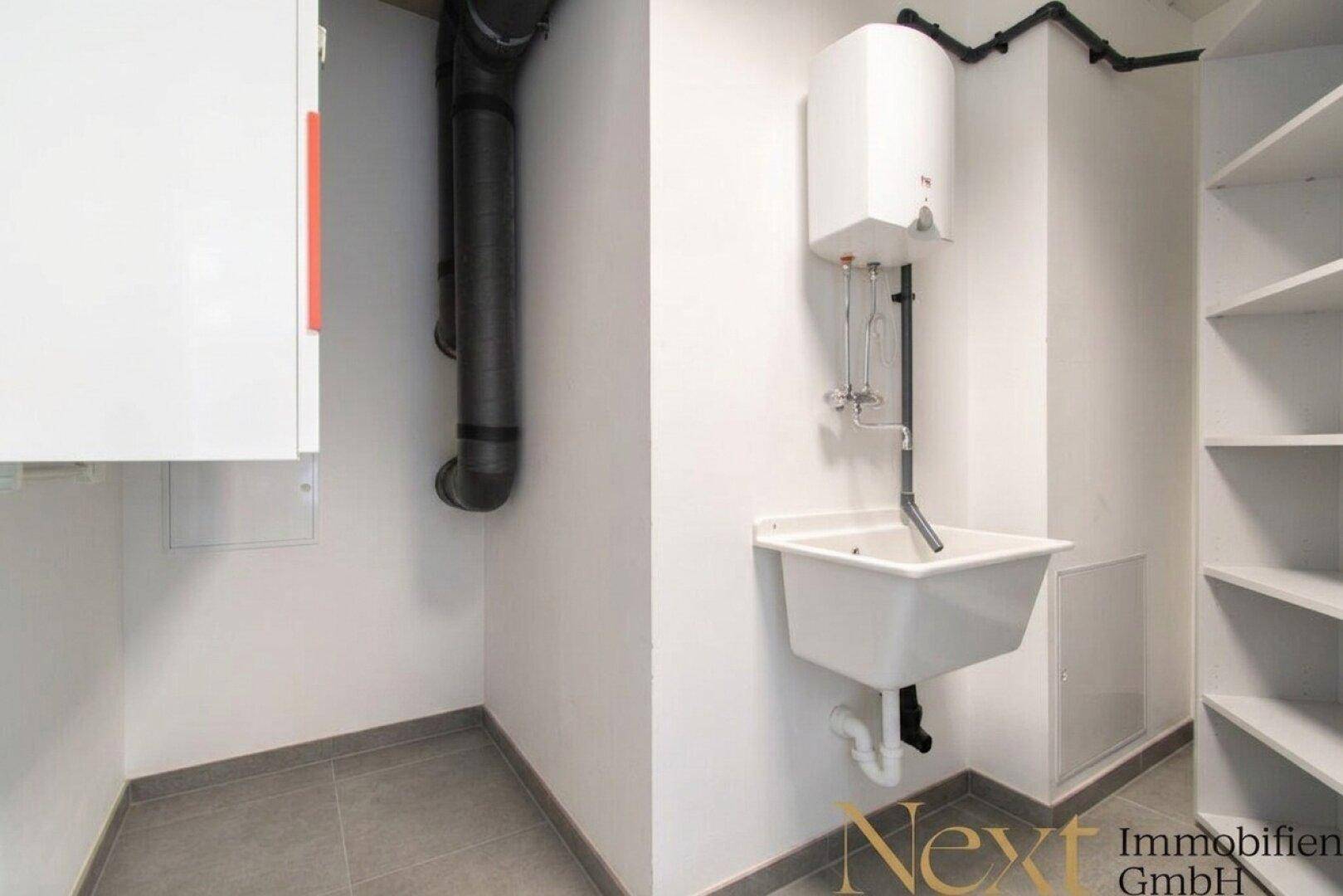 Praktischer Hauswirtschaftsraum mit Waschbecken, Warmwasserbereiter, Regalen und sichtbaren Rohrleitungen.