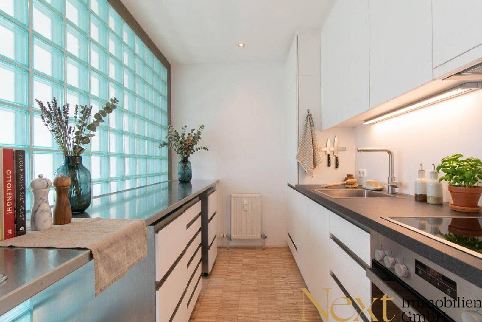 Moderne Küche mit weißen Schränken, dunklen Arbeitsplatten und einer dekorativen Glasbausteinwand.