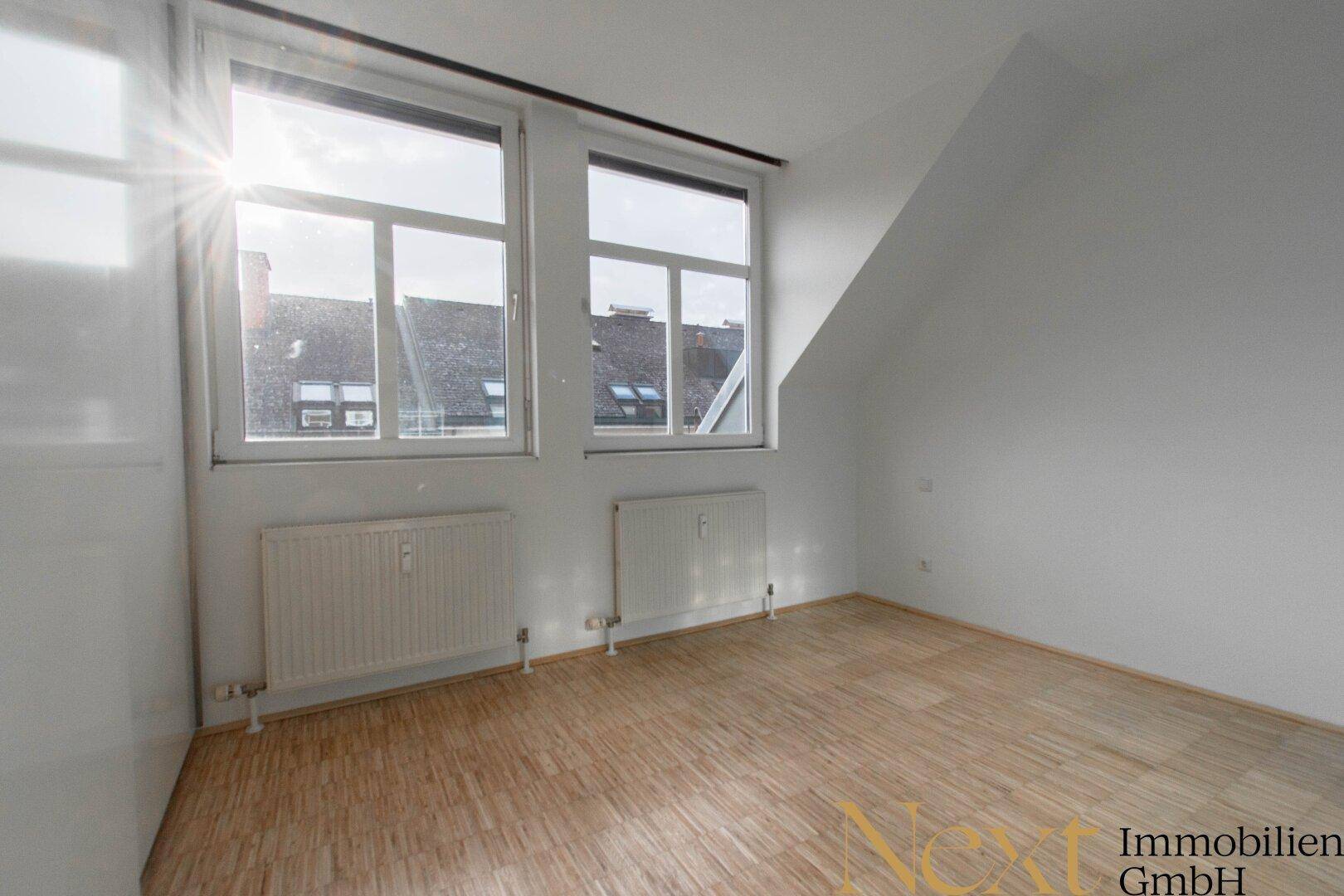 Leeres Schlafzimmer mit Holzboden, Dachschräge und großen Fenstern, bietet viel natürliches Licht.