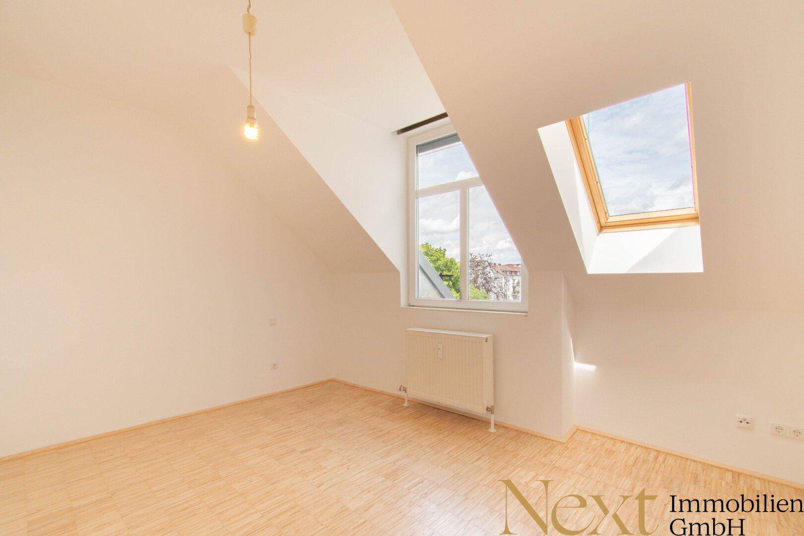Leeres Schlafzimmer mit Holzboden, Dachschräge, Fenster und Dachfenster, bietet viel Tageslicht.