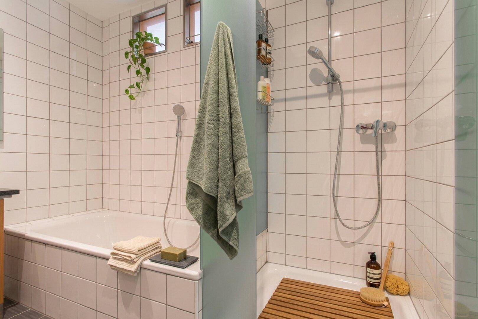 Gefliestes Badezimmer mit Badewanne und separatem Duschbereich, ausgestattet mit kleinen Fenstern.