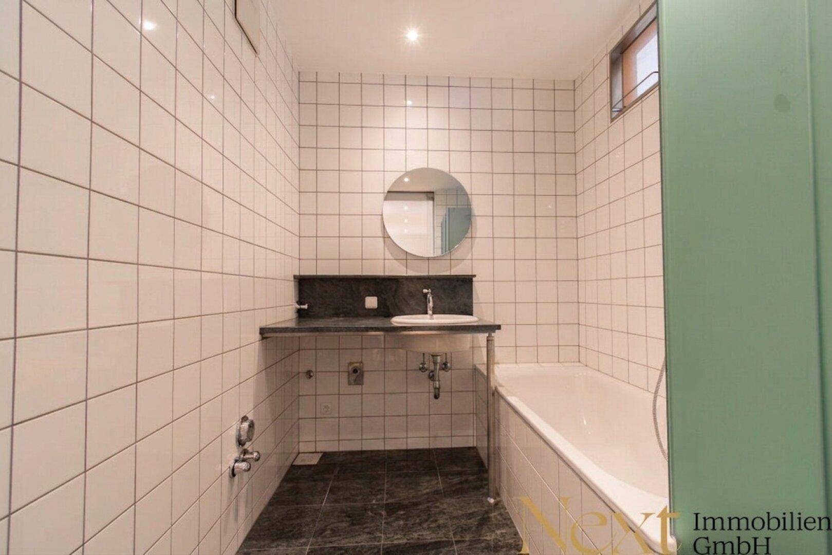 Leeres Badezimmer mit weißen Fliesen, Badewanne und Waschbeckenbereich, bereit zur Einrichtung.