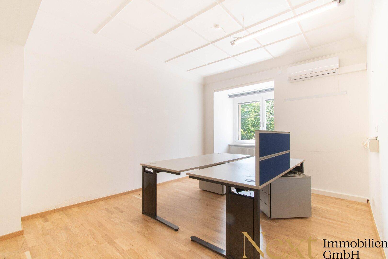 Modernes Büro mit zwei Schreibtischen, Klimaanlage und hellem Holzfußboden.