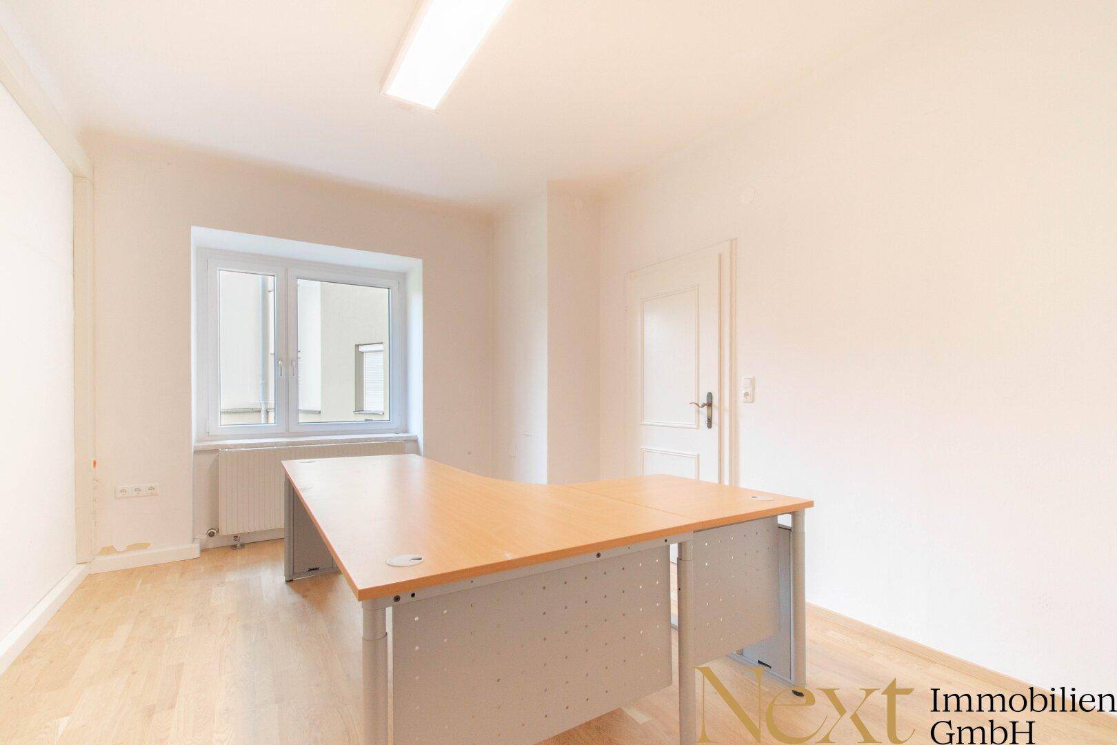 Einzelbüro mit großem Eckschreibtisch, Holzboden und einem Fenster.