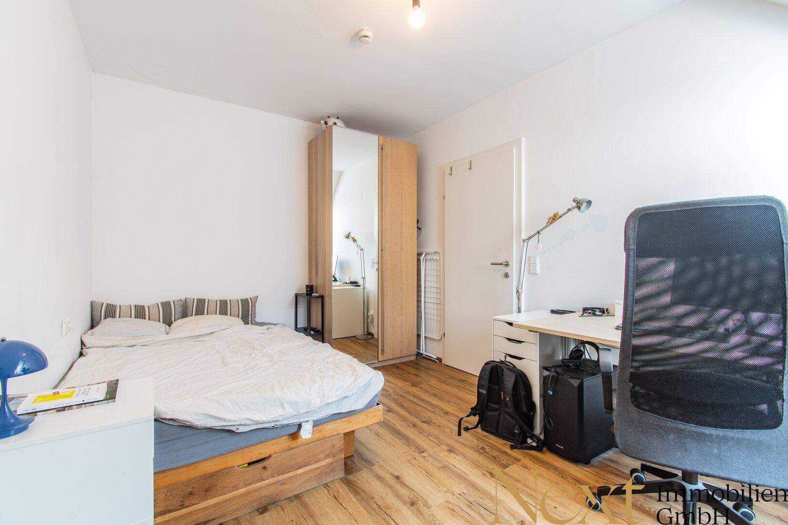 Schlafzimmer mit Holzbett, Schreibtisch und Spiegelschrank, ideal für Studenten oder Gäste.