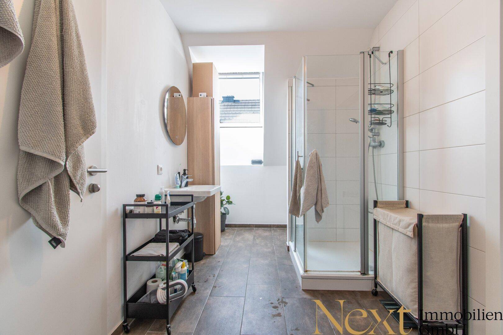 Modernes Badezimmer mit Duschkabine, Waschbecken und dunklen Bodenfliesen.