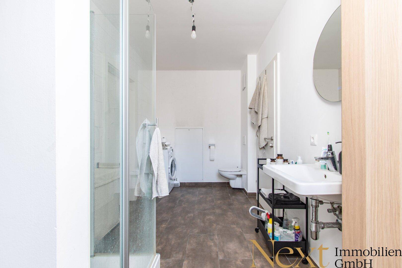 Helles Badezimmer mit Duschkabine, WC, Waschbecken und Platz für eine Waschmaschine.