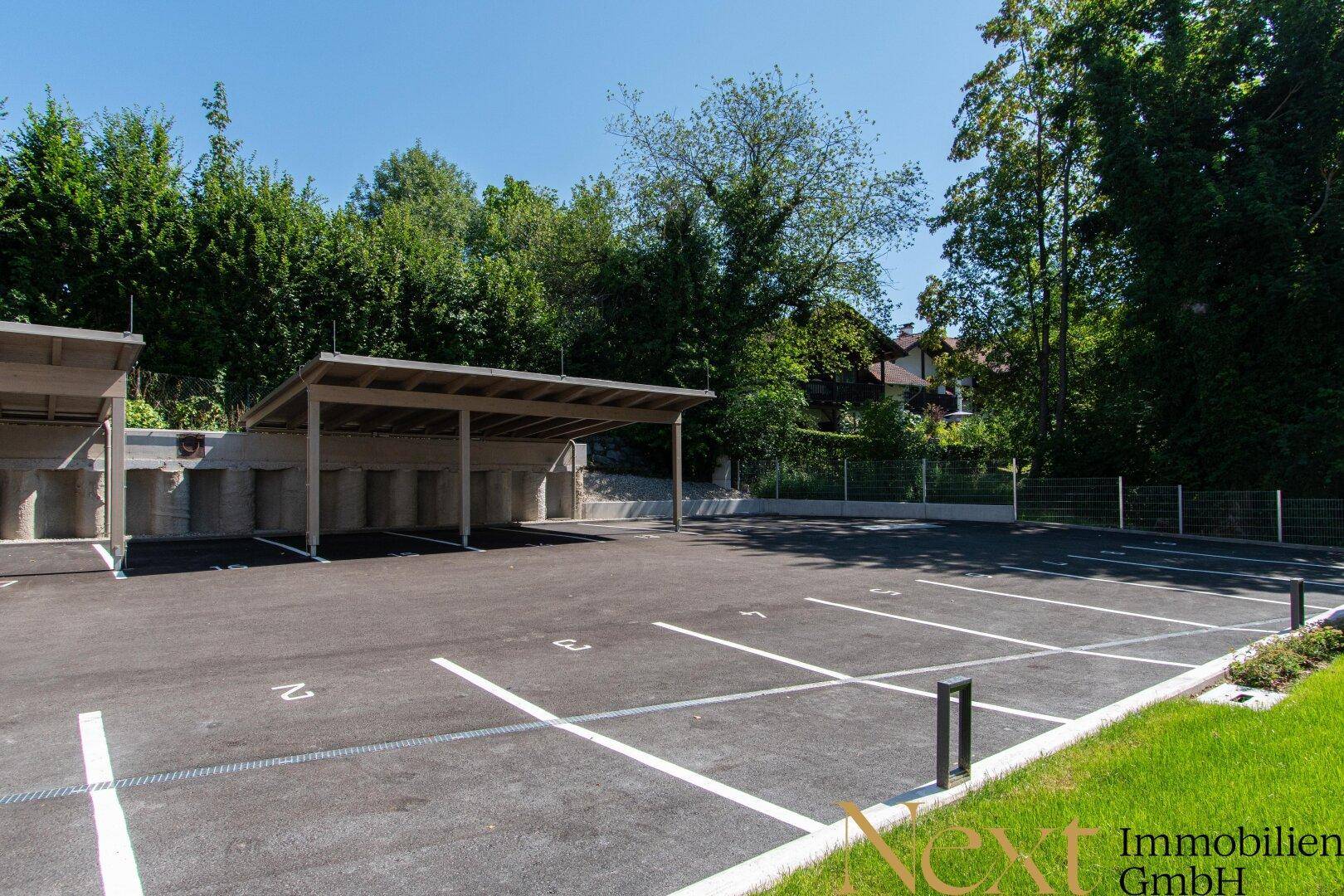 Großer Außenparkplatz mit mehreren Stellplätzen und einem überdachten Carport.