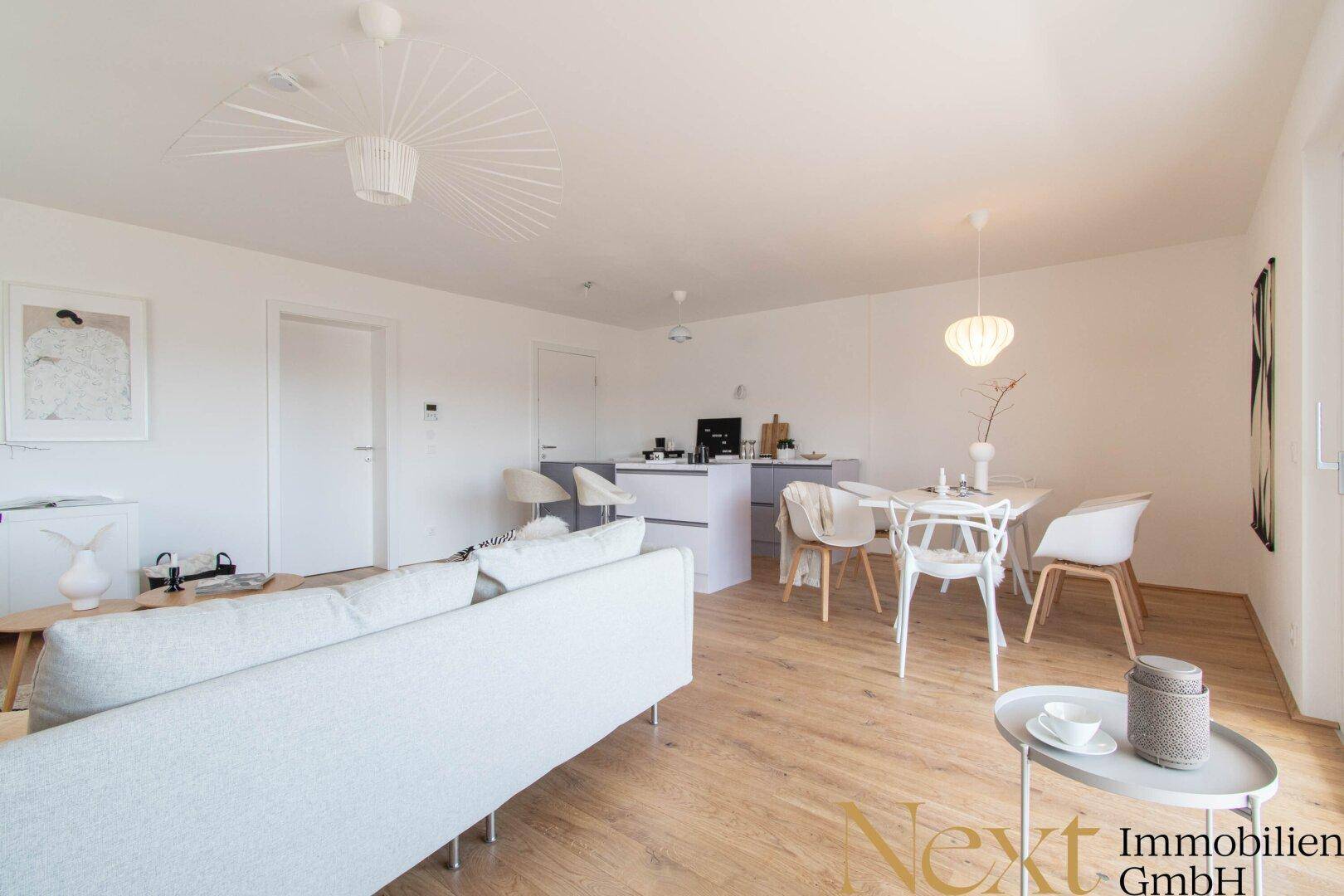 Gemütlicher Wohnbereich mit hellem Sofa und Holzboden, offen zum Ess- und Küchenbereich.