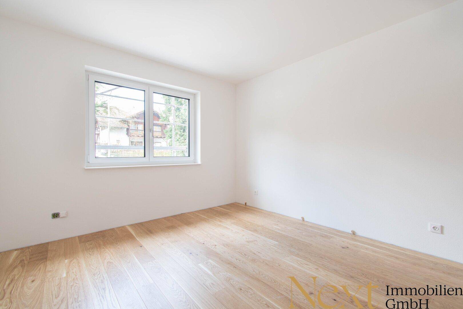 Leeres Schlafzimmer mit hellem Holzboden und großem Fenster, ideal für individuelle Gestaltung.