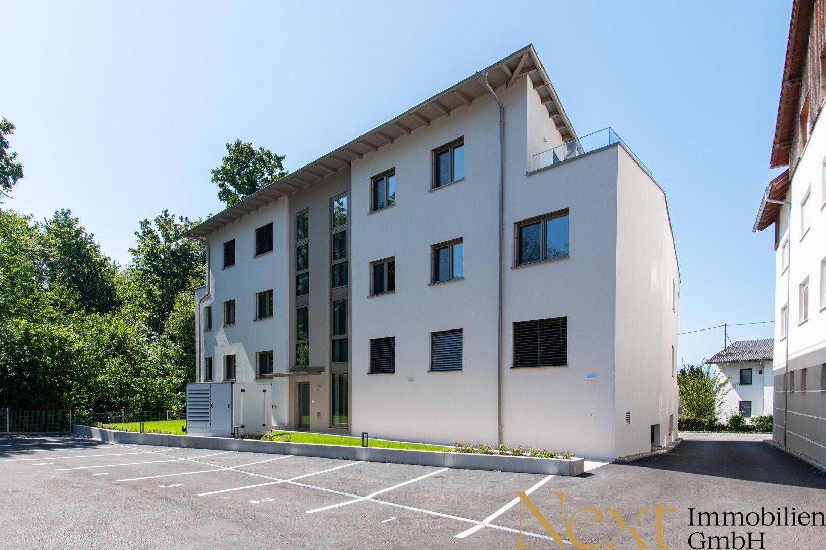 Rückansicht des modernen Gebäudes mit Jalousien an den Fenstern und einem großen Außenparkplatz.