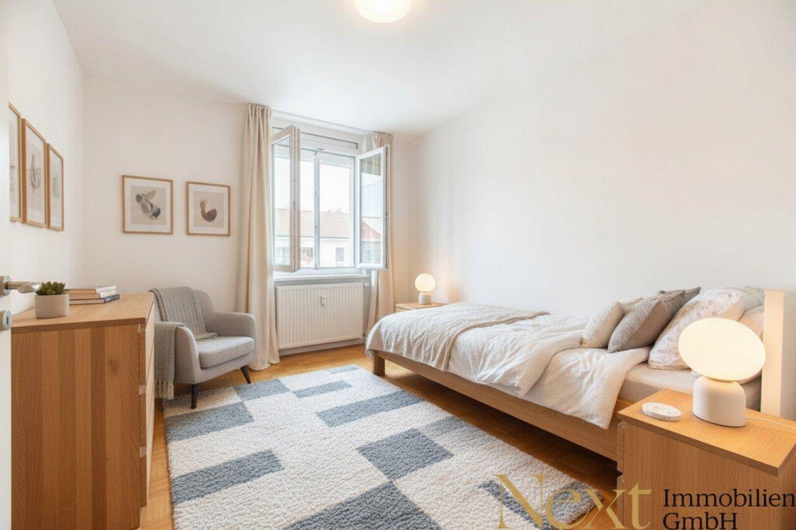 Freundliches Schlafzimmer mit Einzelbett, Sessel und Holzkommode, durch das Fenster fällt viel Licht.