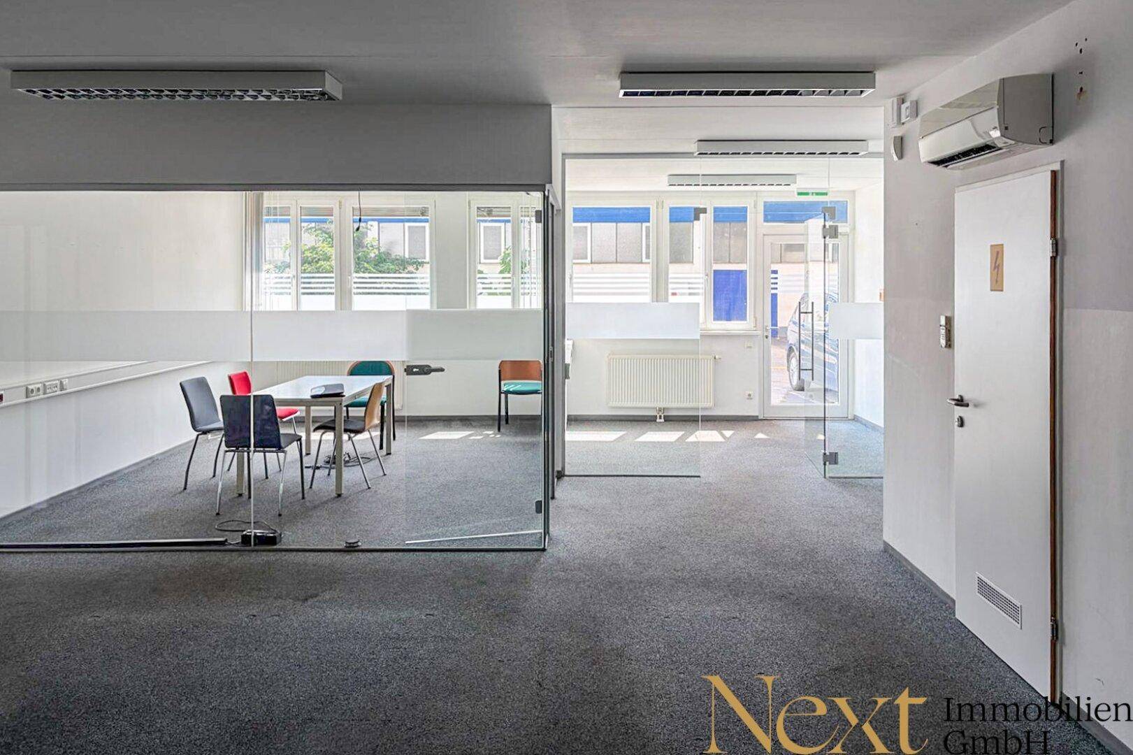 Modernes Büro mit Glaswänden, Teppichboden und einem Besprechungsbereich, ausgestattet mit Klimaanlage.