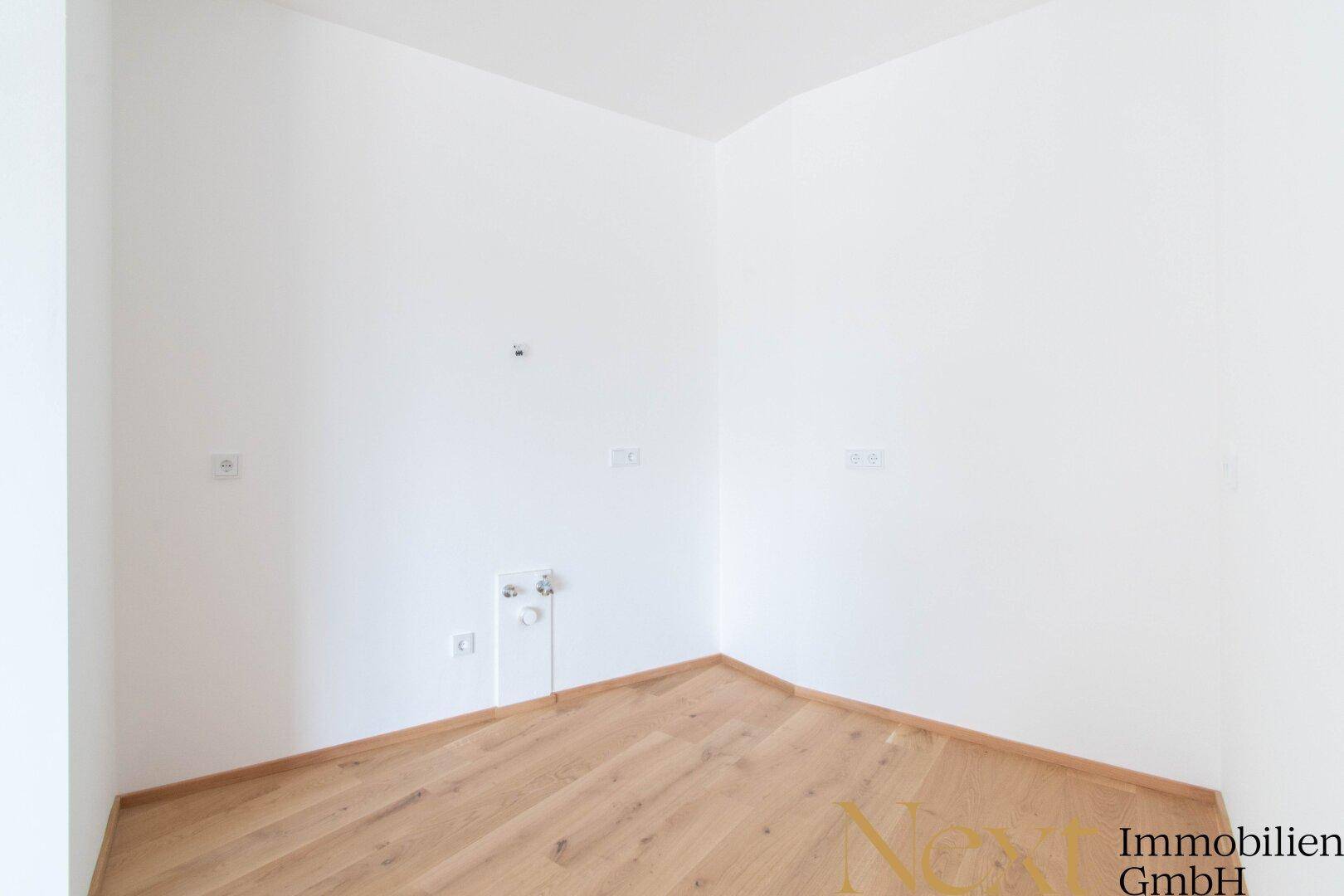 Leere Küchenecke mit Holzboden und Anschlüssen für eine Einbauküche, bereit zur Gestaltung.