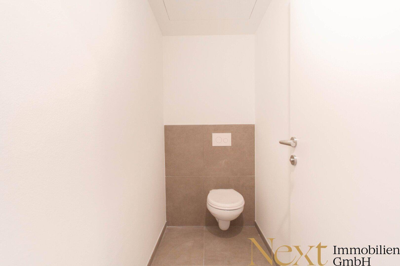 Kleines Gäste-WC mit wandhängender Toilette und modernen Fliesen im unteren Bereich.