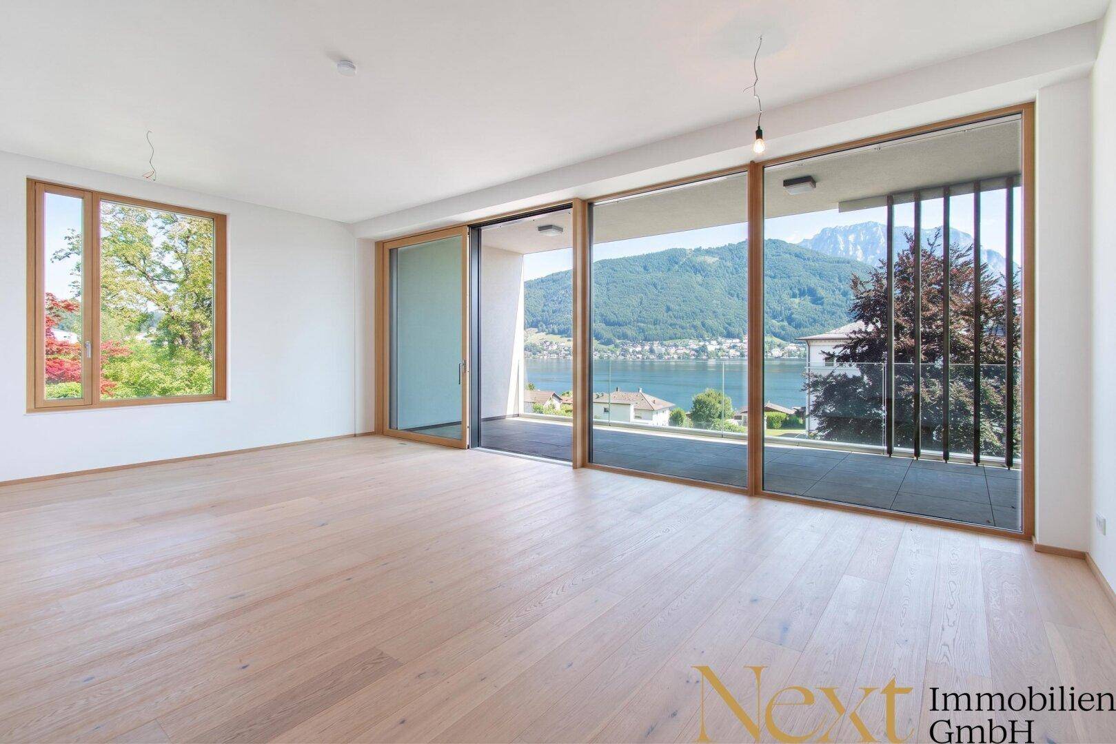 Geräumiges, leeres Wohnzimmer mit großen Fenstern, Seeblick und Zugang zur Terrasse.