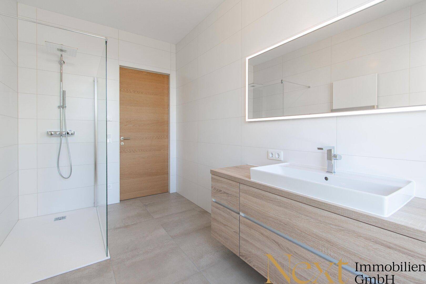Modernes Badezimmer mit ebenerdiger Dusche, großem Waschtisch und beleuchtetem Spiegel.