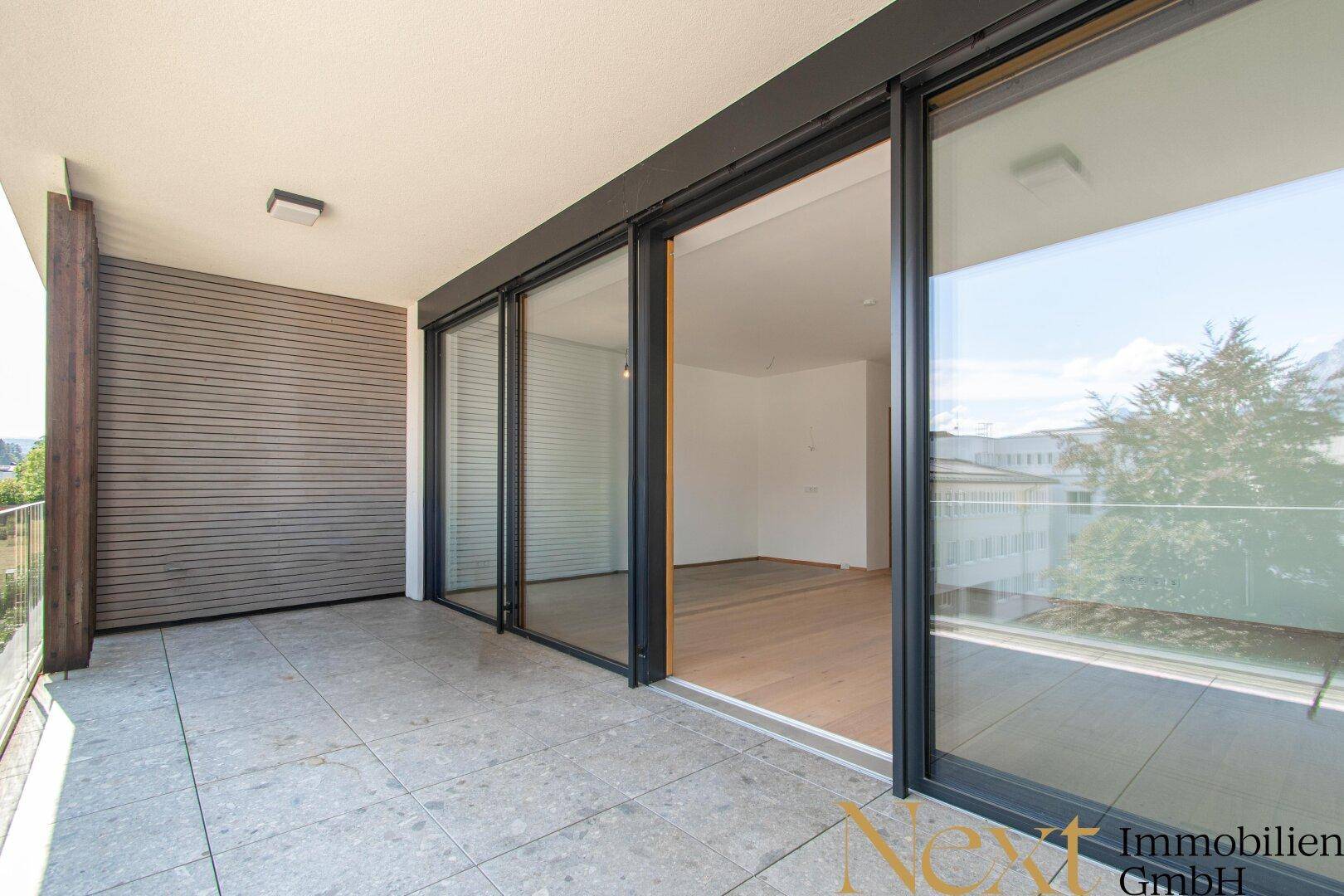 Geräumige, geflieste Terrasse mit Schiebetüren zum hellen, leeren Wohnzimmer.
