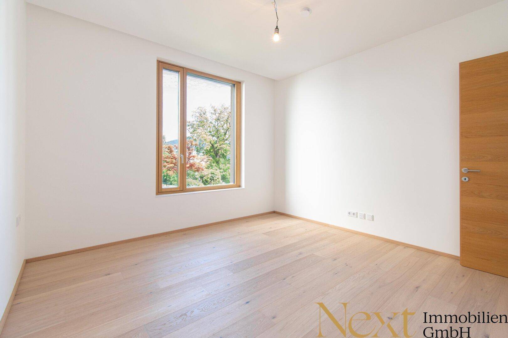 Helles, leeres Schlafzimmer mit großem Fenster und Parkettboden.