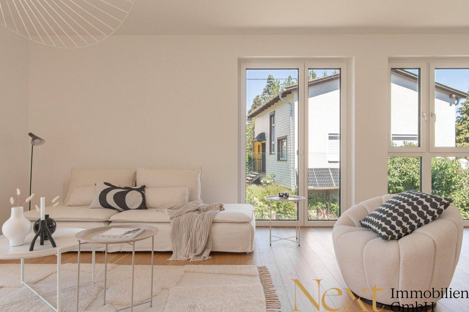 Gemütlicher Wohnbereich mit beigem Sofa und Sessel, großen Fenstern und Blick auf die Nachbarschaft.