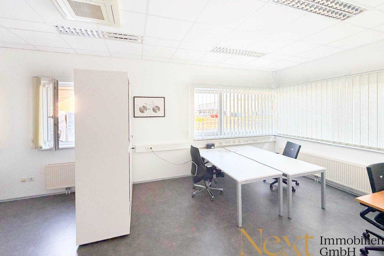 Funktionaler Bürobereich mit zwei Arbeitsplätzen, großen Fenstern und Jalousien für angenehmes Arbeitslicht.