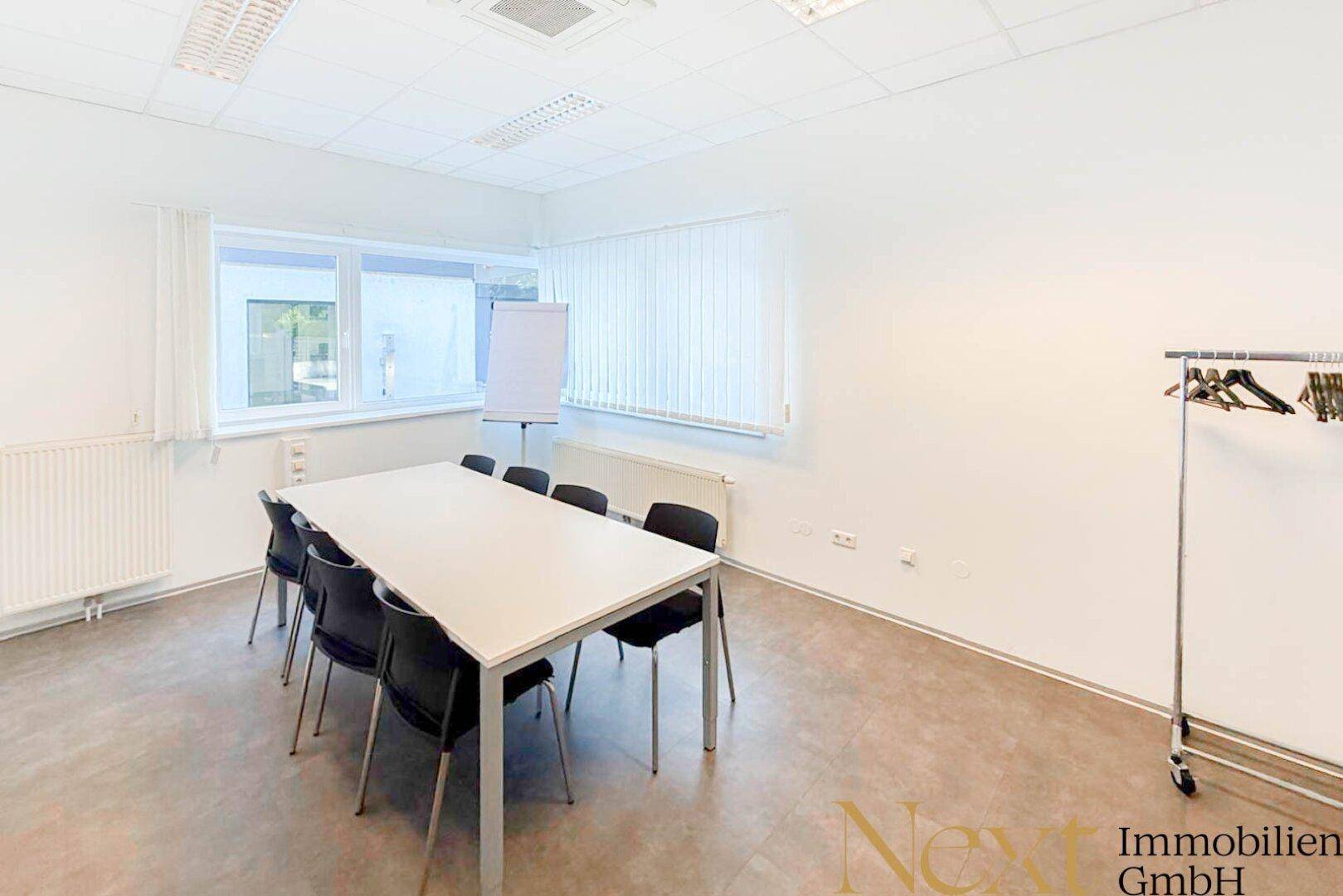 Geräumiger Konferenzraum mit großem Besprechungstisch, Whiteboard und Garderobe, ideal für Teammeetings.