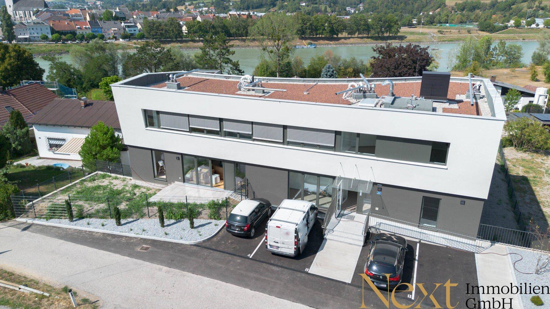 Modernes Gebäude mit Flachdach, großen Fenstern und ausreichend Parkplätzen vor dem Eingang.
