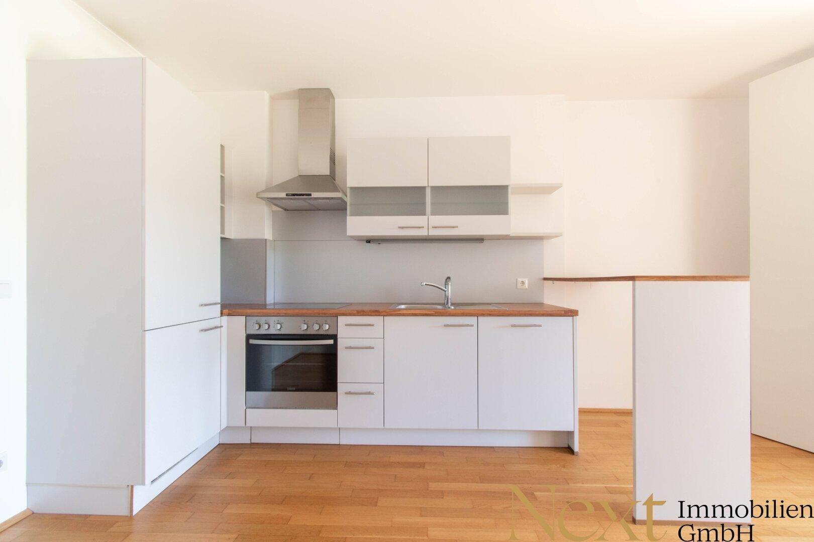 Moderne Einbauküche mit weißen Schränken, Holz-Arbeitsplatte und integrierten Geräten.