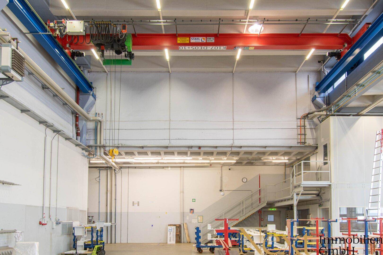 Weitläufige Industriehalle mit Kranbahn, Treppenaufgang und hohen Decken.