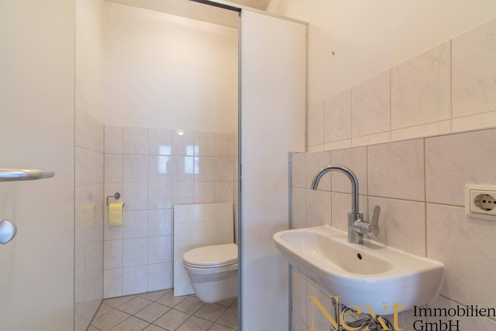 Kleine Gästetoilette mit Waschbecken, WC und hellen Fliesen an Wänden und Boden.