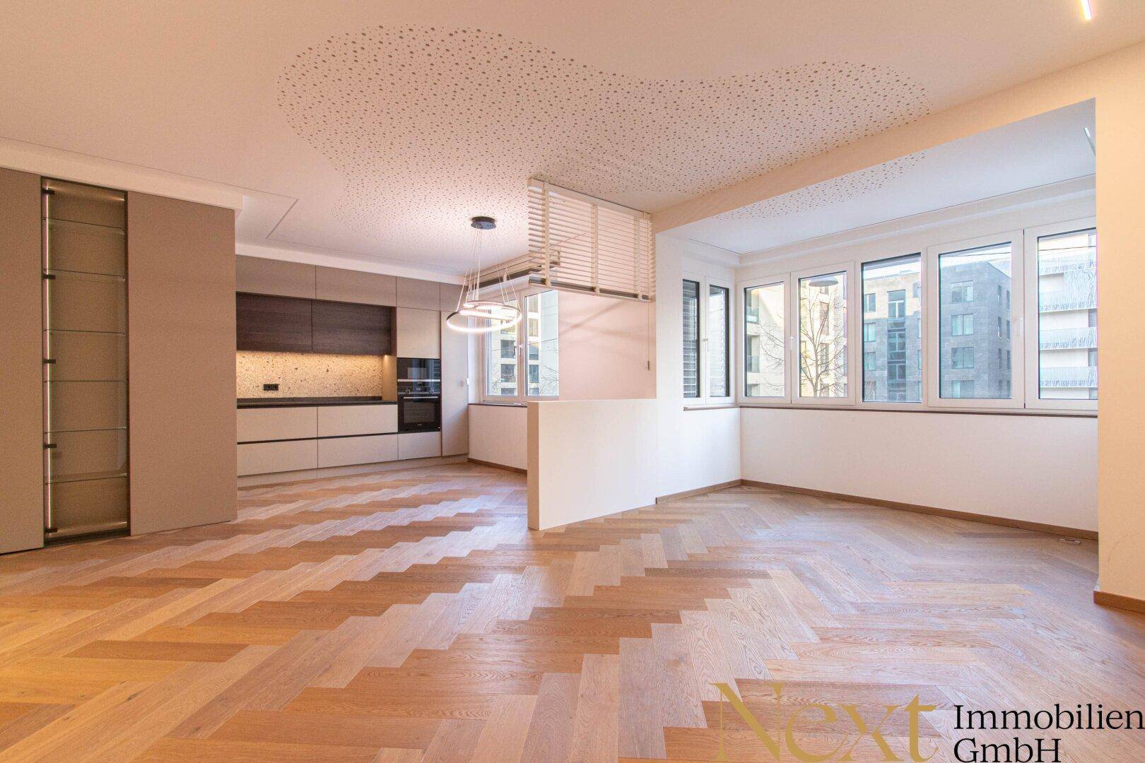 Geräumiger, leerer Wohn- und Essbereich mit offener Küche und elegantem Fischgrätparkett.