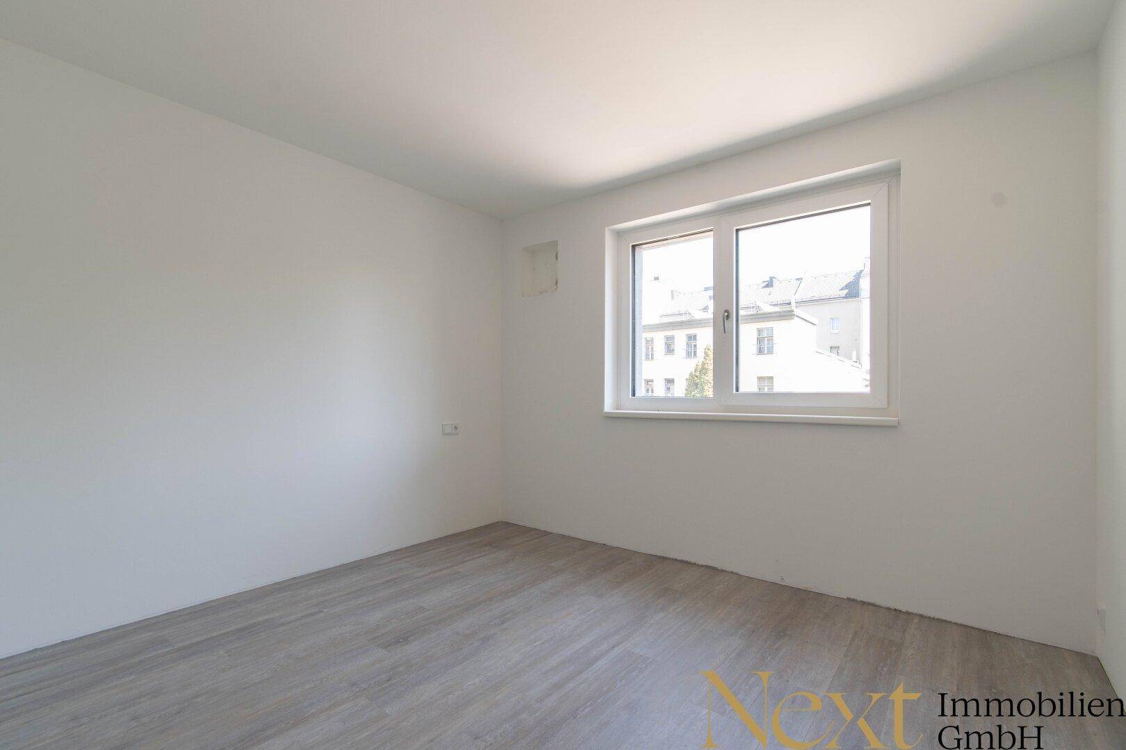 Leeres Schlafzimmer mit hellem Laminatboden und einem Fenster zur Straße.