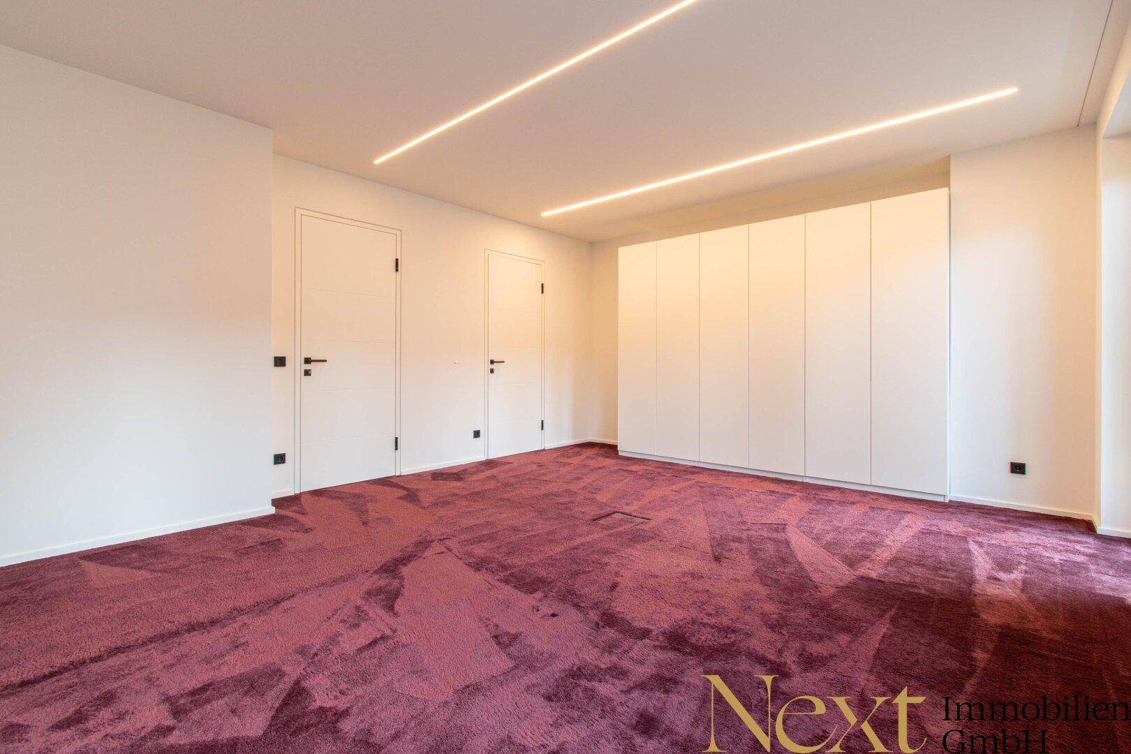Geräumiges Schlafzimmer mit weißem Einbauschrank, lila Teppichboden und zwei Türen.