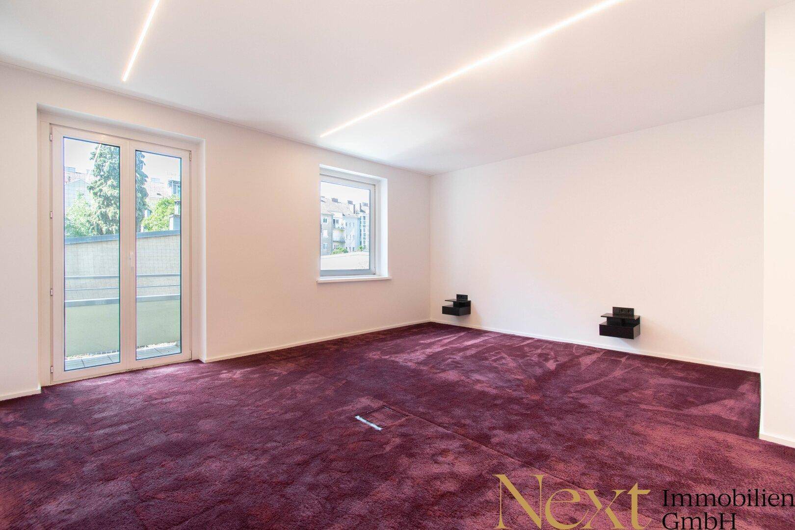Leeres Schlafzimmer mit lila Teppichboden, großen Fenstern und Balkonzugang.