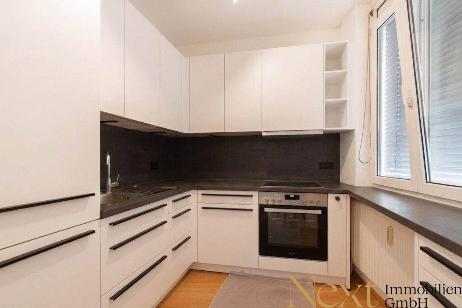 Moderne Einbauküche mit weißen Schränken, dunkler Arbeitsplatte und integrierten Geräten.