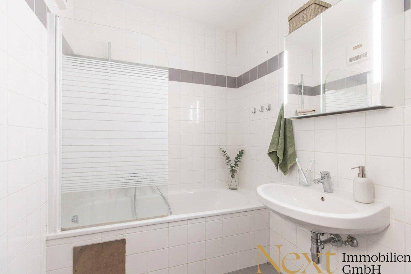 Gefliestes Badezimmer mit Badewanne, Duschabtrennung und Waschbecken, in gutem Zustand.