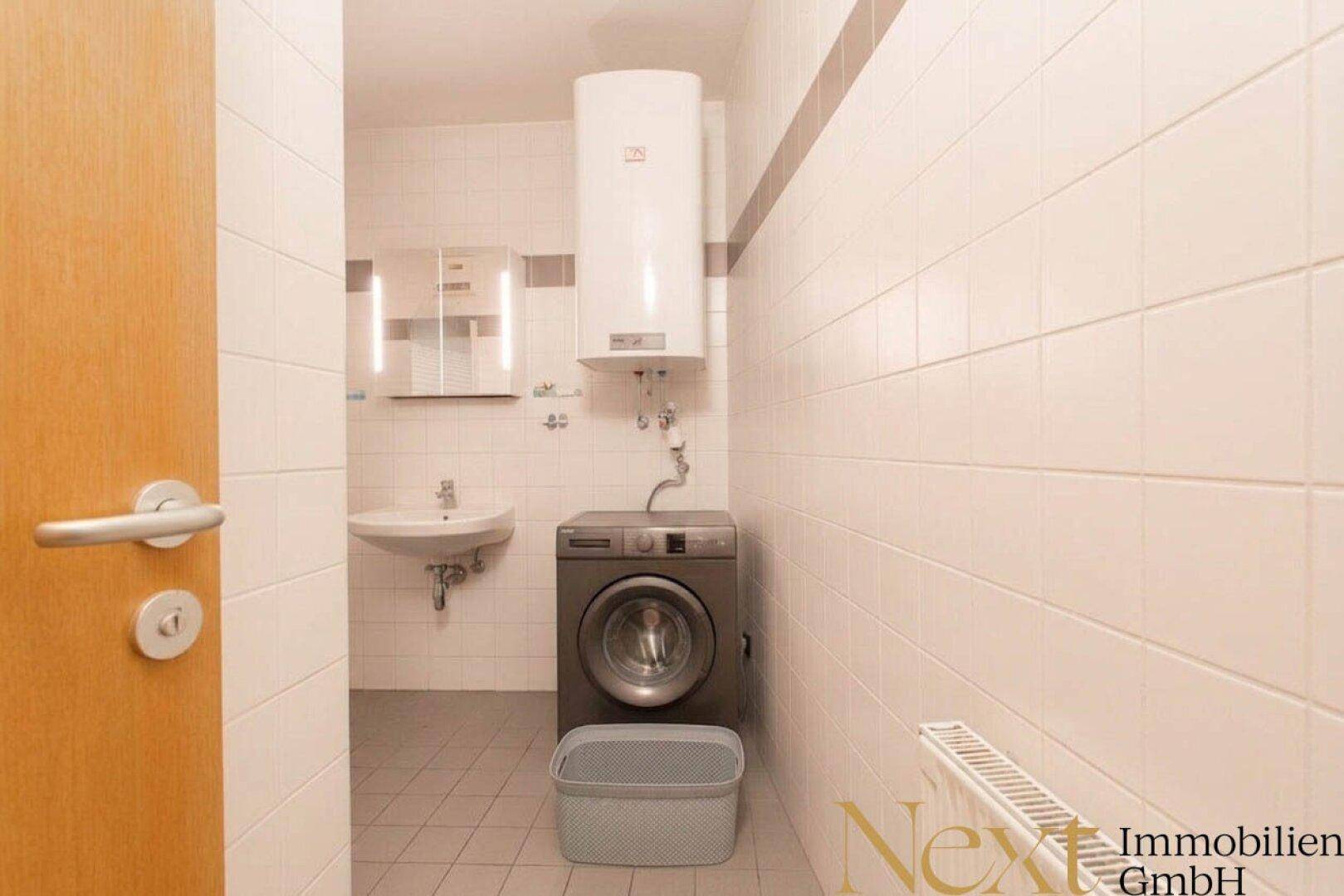 Praktischer Hauswirtschaftsraum mit Waschmaschine, Waschbecken und Warmwasserbereiter, funktional und sauber.