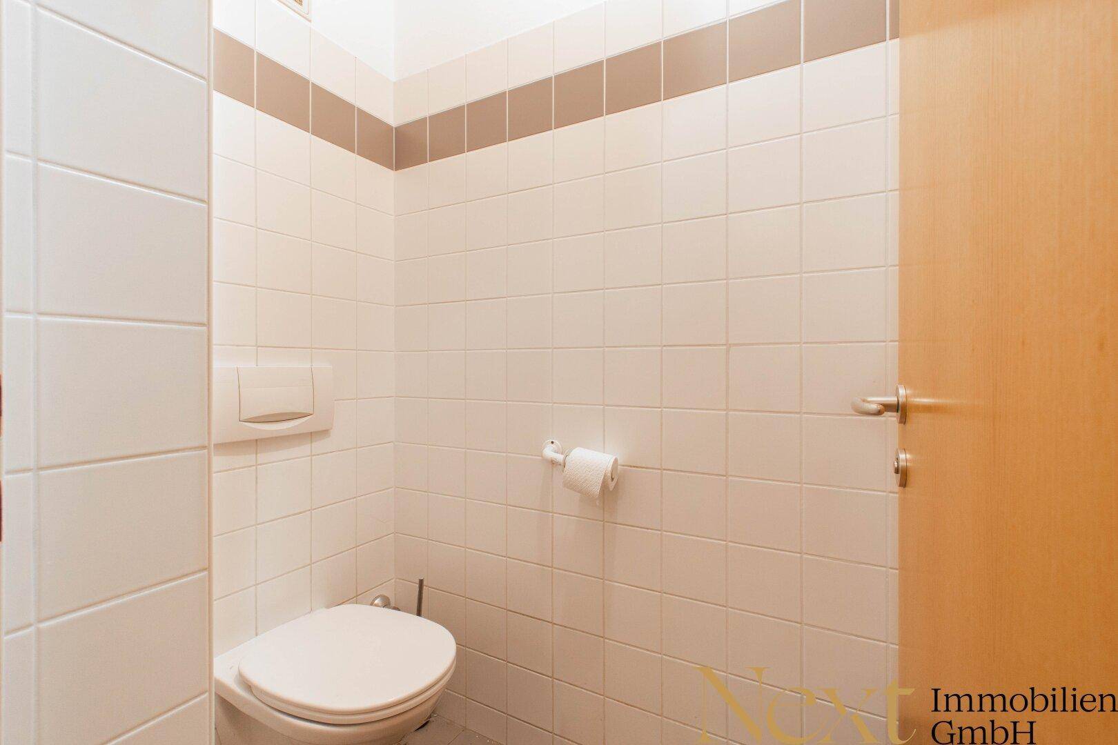 Separates WC mit Wand-WC und Fliesen an den Wänden, sauber und gepflegt.