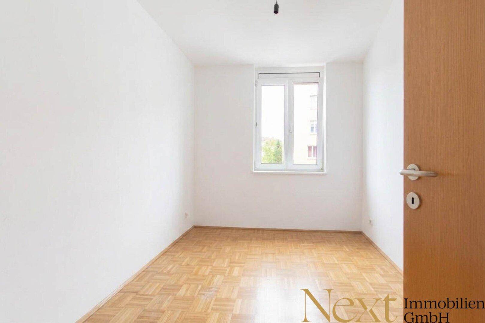 Leeres Zimmer mit Parkettboden und Fenster, ideal als Kinderzimmer oder Büro nutzbar.