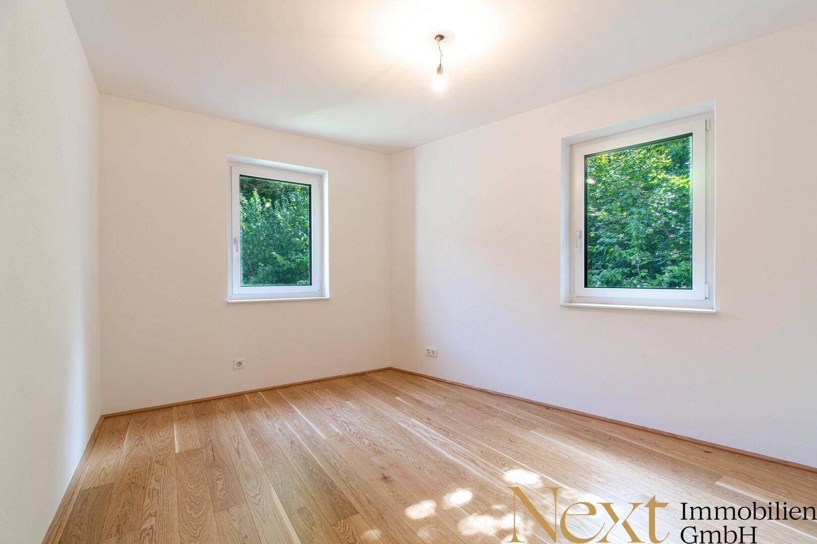 Geräumiges, leeres Schlafzimmer mit zwei Fenstern und Holzboden, bietet viel Licht.