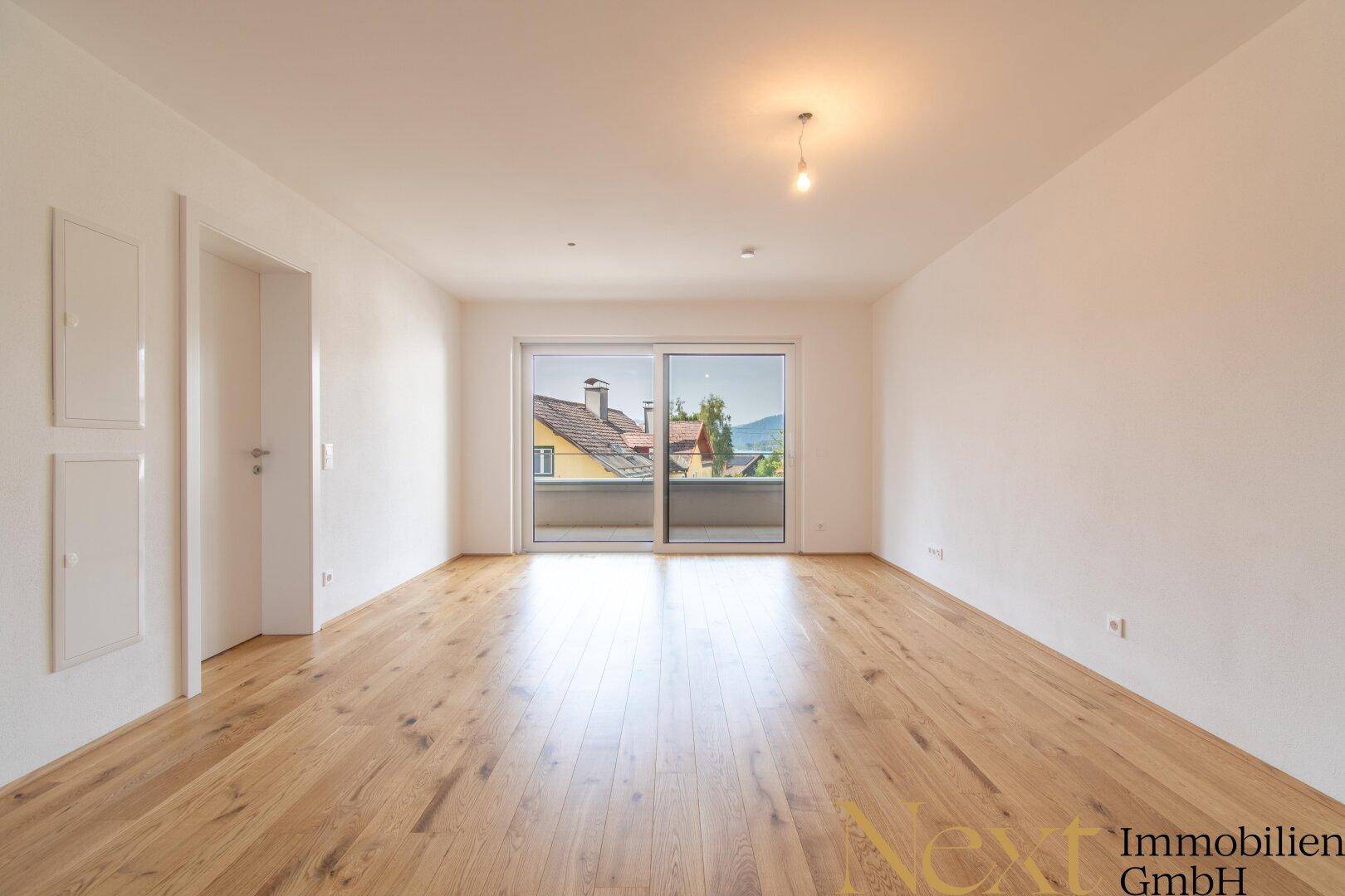 Helles, leeres Zimmer mit Eichenparkett und großer Schiebetür zum Balkon, bietet viel Tageslicht.