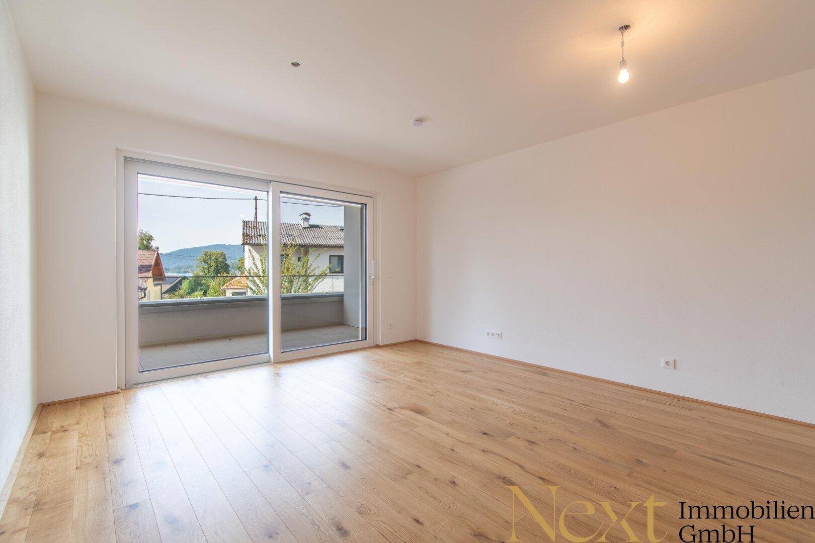 Geräumiges Zimmer mit hellem Holzfußboden und Zugang zu einem sonnigen Balkon.